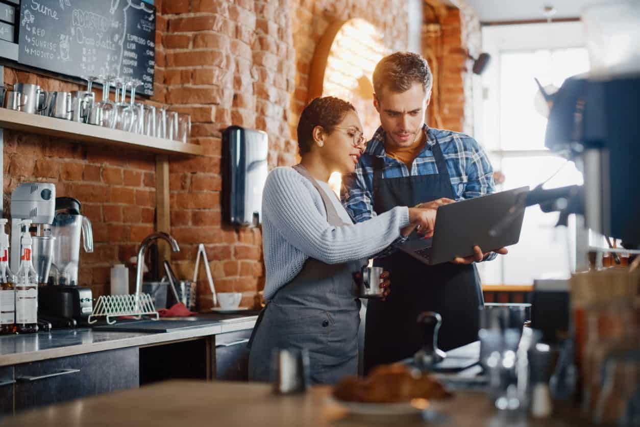 two people working in a coffee house and talking over a computer